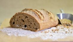 Artisan bread loaf on wooden board with scattered flour and grains